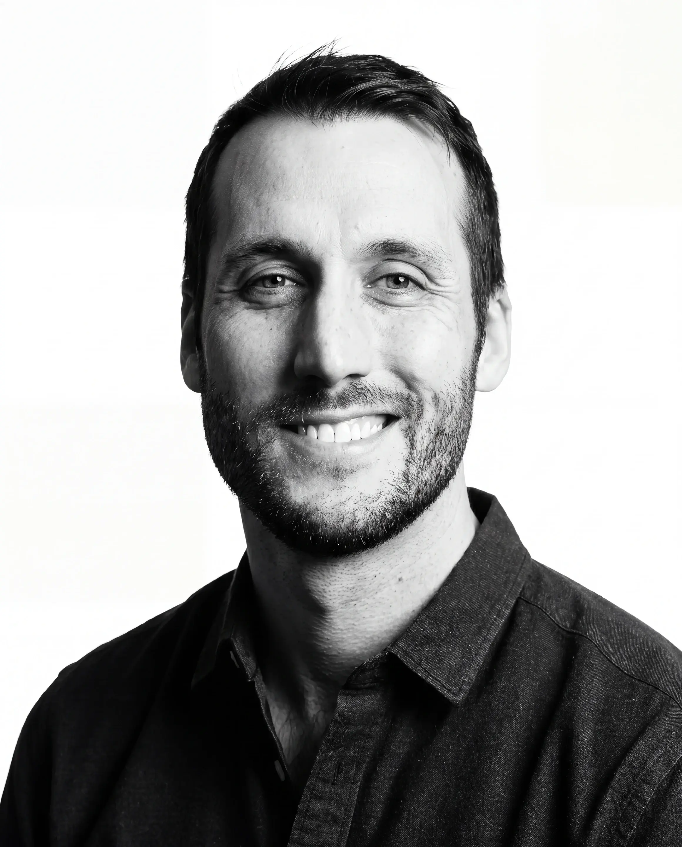 Black and white headshot portrait of man with beard wearing dark collared shirt.