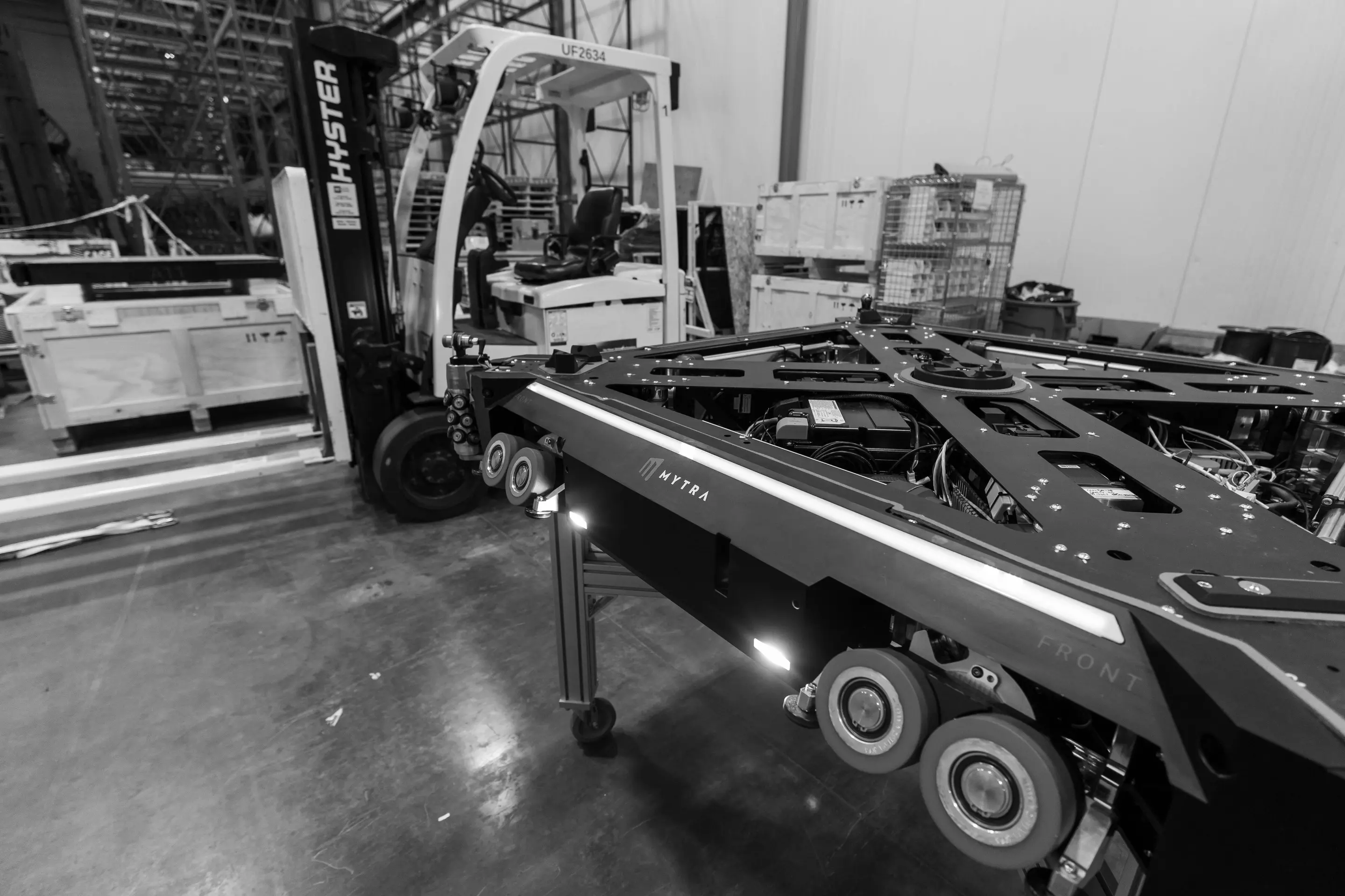 Industrial warehouse scene showing forklift and large equipment transport trailer.