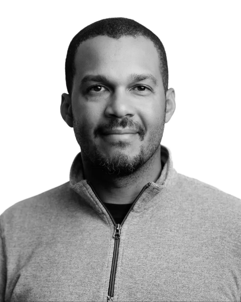 Black and white headshot portrait of a man in a zippered collared jacket against white background.