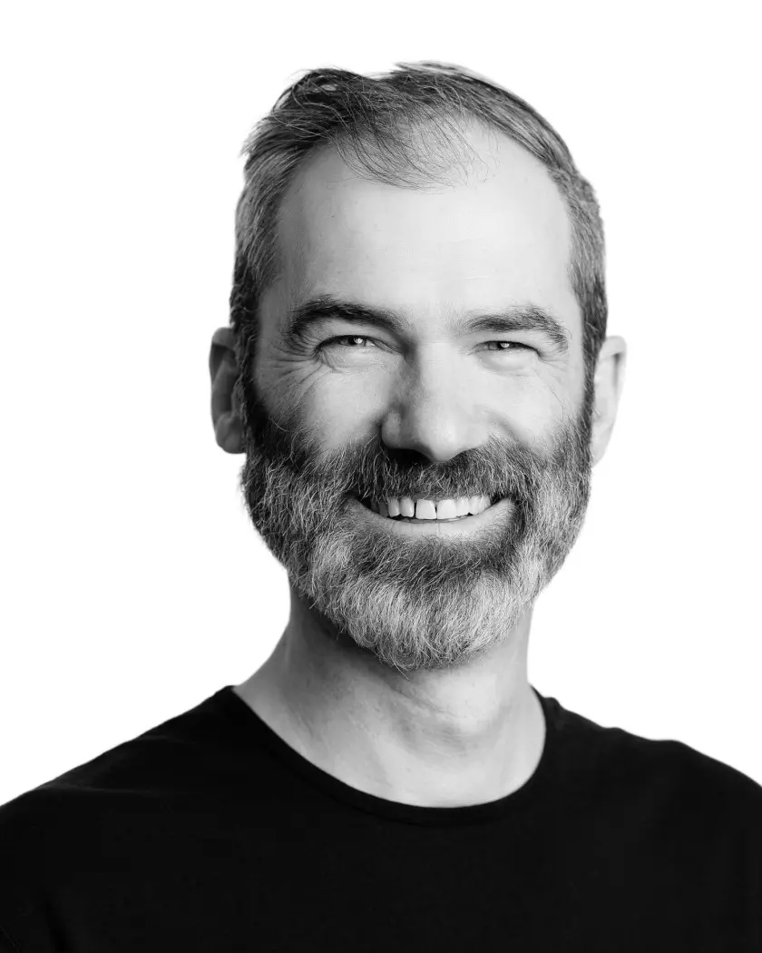 Black and white headshot portrait of a man with full beard smiling widely, against white background.