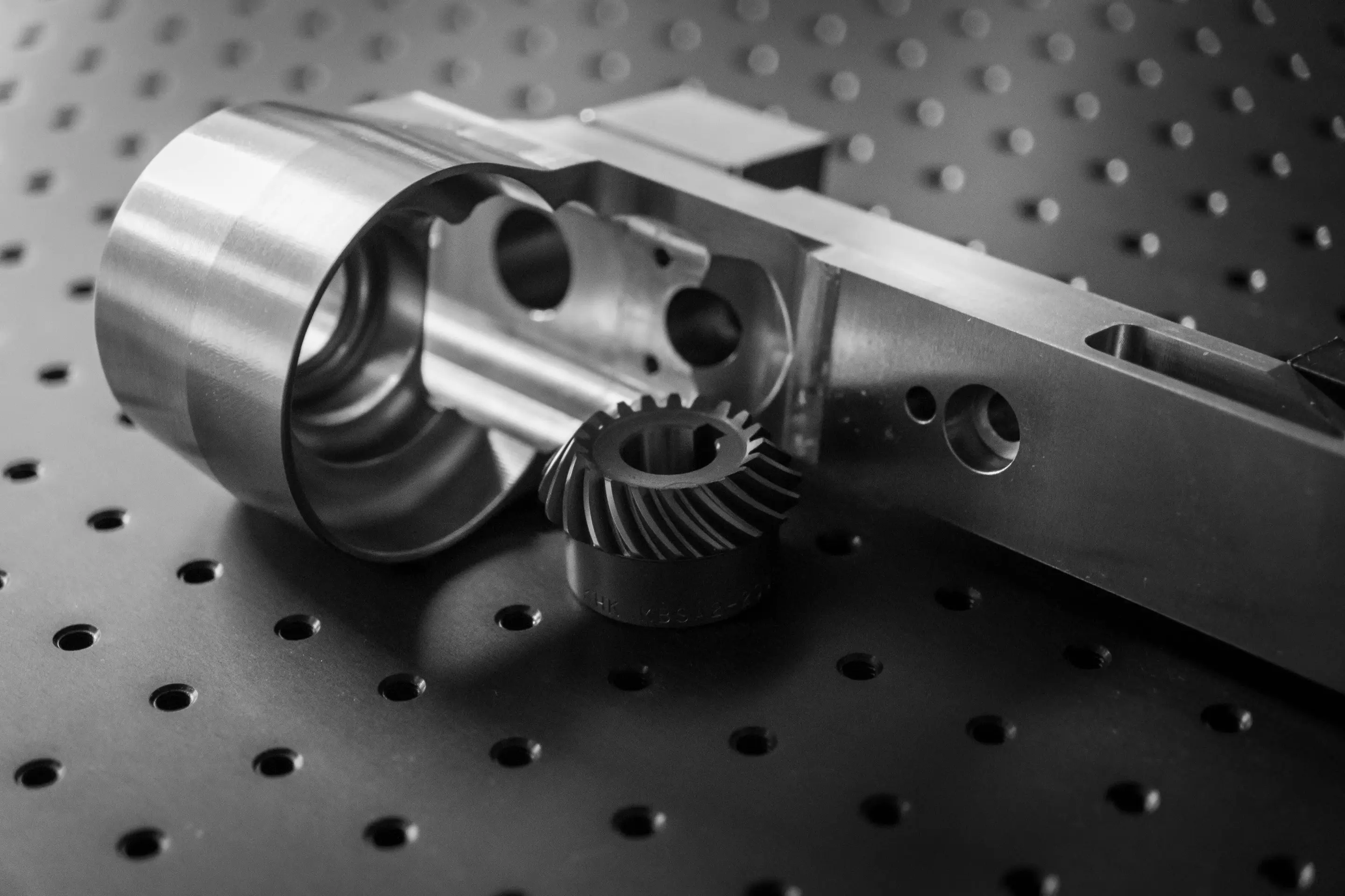 Close-up of metal machinery parts with gear and cylindrical components on perforated surface.